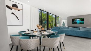 A modern dining area with a glass table and quilted chairs, a blue sofa, and a TV in the living room. - Atlantic Silent Heights Villa (Adeje)