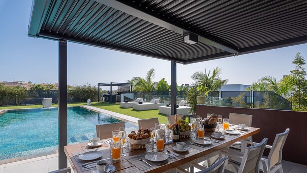 A dining table set for breakfast with a view of a swimming pool and a garden. - Atlantic Silent Heights Villa (Adeje)