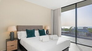 A modern hotel room with a large bed, two bedside tables with lamps, a view of the city through floor-to-ceiling windows, and a balcony with a view of the sea. - Atlantic Silent Heights Villa (Adeje)