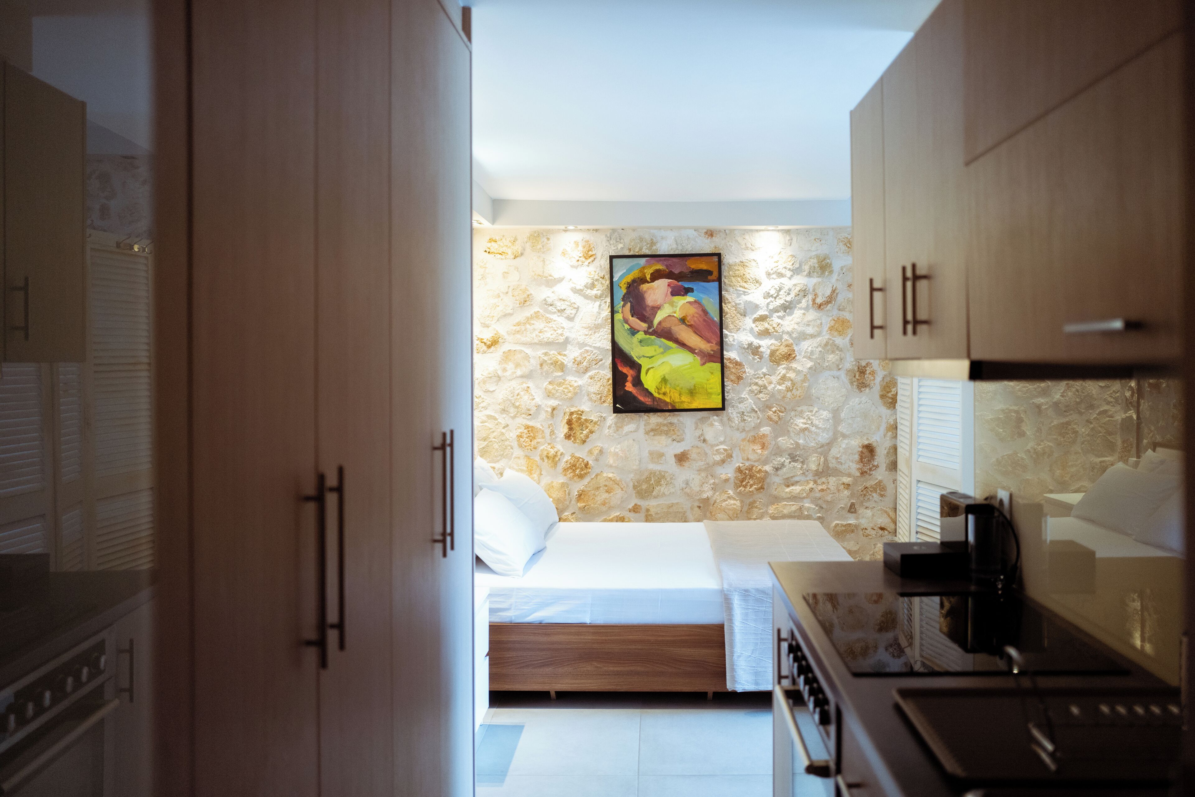 Une chambre à coucher de taille réduite, comprenant un lit, un tableau accroché au mur et un coin cuisine.