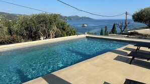 A swimming pool with clear blue water, surrounded by greenery and overlooking a scenic view of the sea and distant hills. - Christie's Luxury Suites (Igoumenitsa)