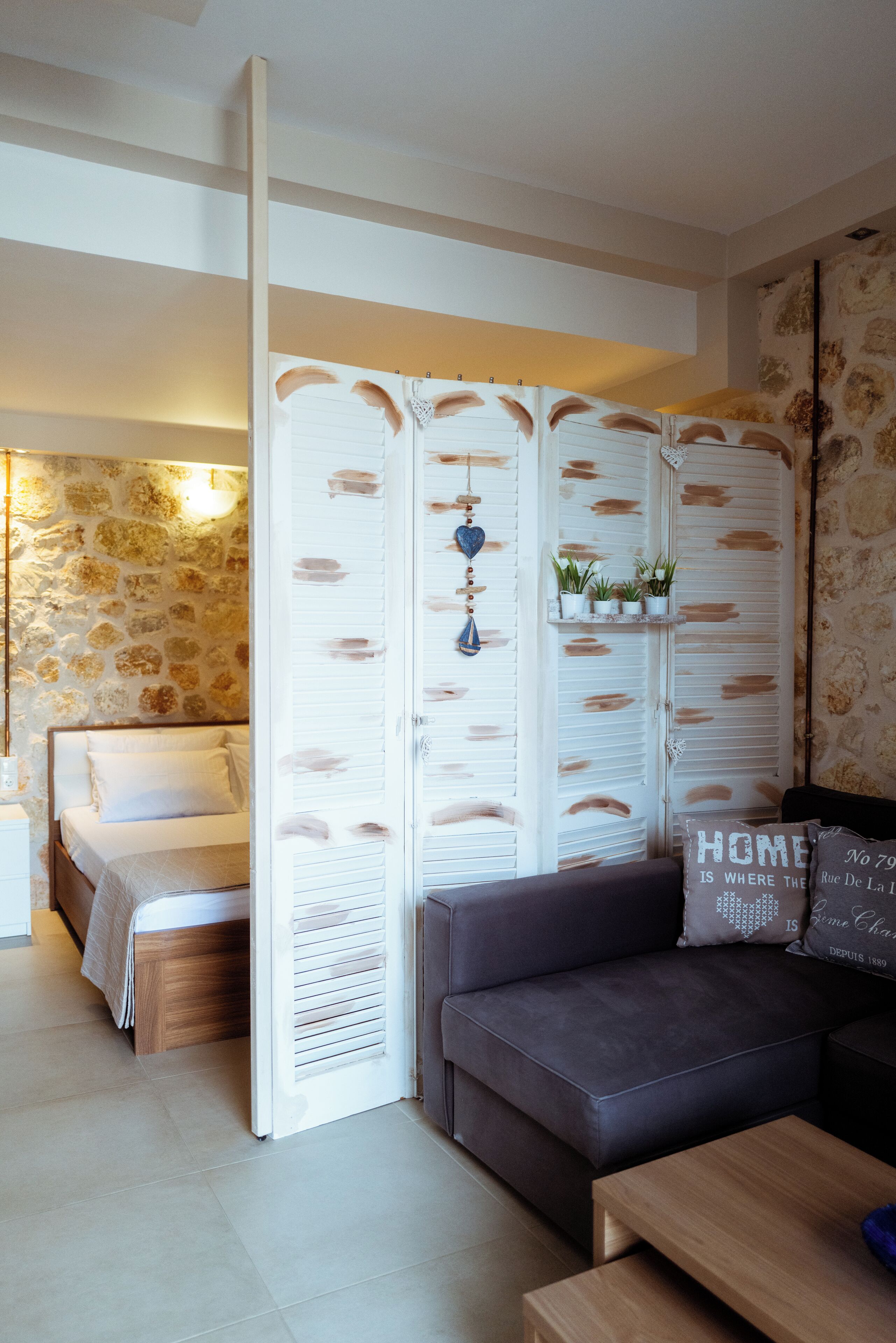 Een moderne slaapkamer met een bed, een grijze bank, een houten bijzettafeltje en een witte roomdivider met decoratieve details.