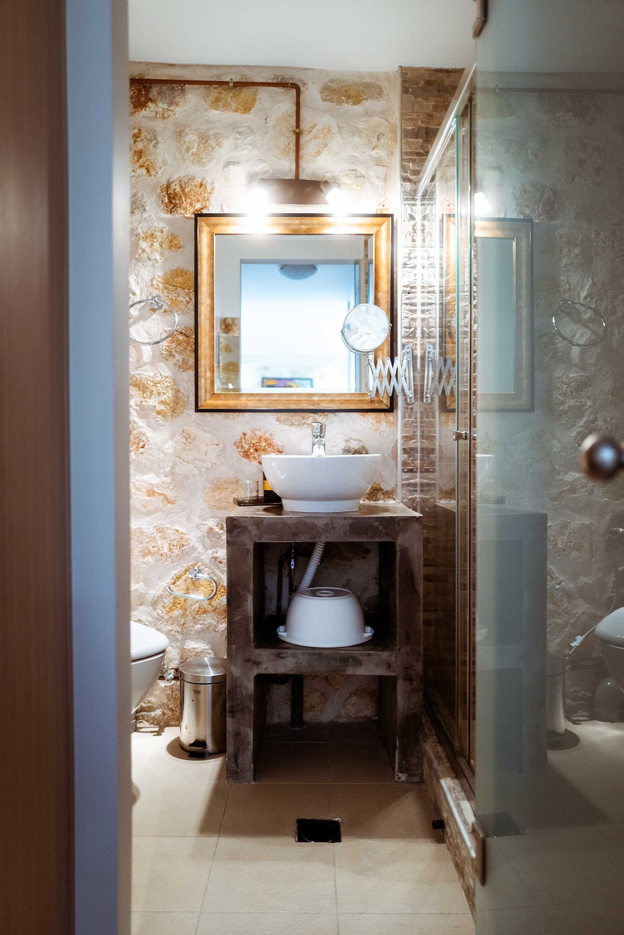 A bathroom with a stone wall, a wooden vanity, a sink, a mirror, and a glass shower enclosure.