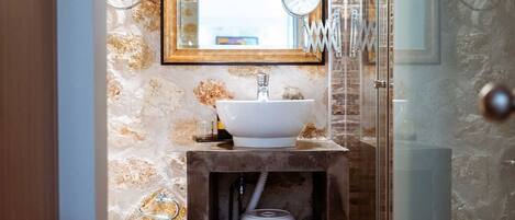 Un baño con pared de piedra, tocador de madera, lavabo, espejo y cabina de ducha con mampara de vidrio.