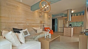 A modern living room with a wooden wall, a sofa with cushions, a coffee table, and a kitchen area with cabinets and a hanging light fixture. - Christie's Luxury Suites (Igoumenitsa)
