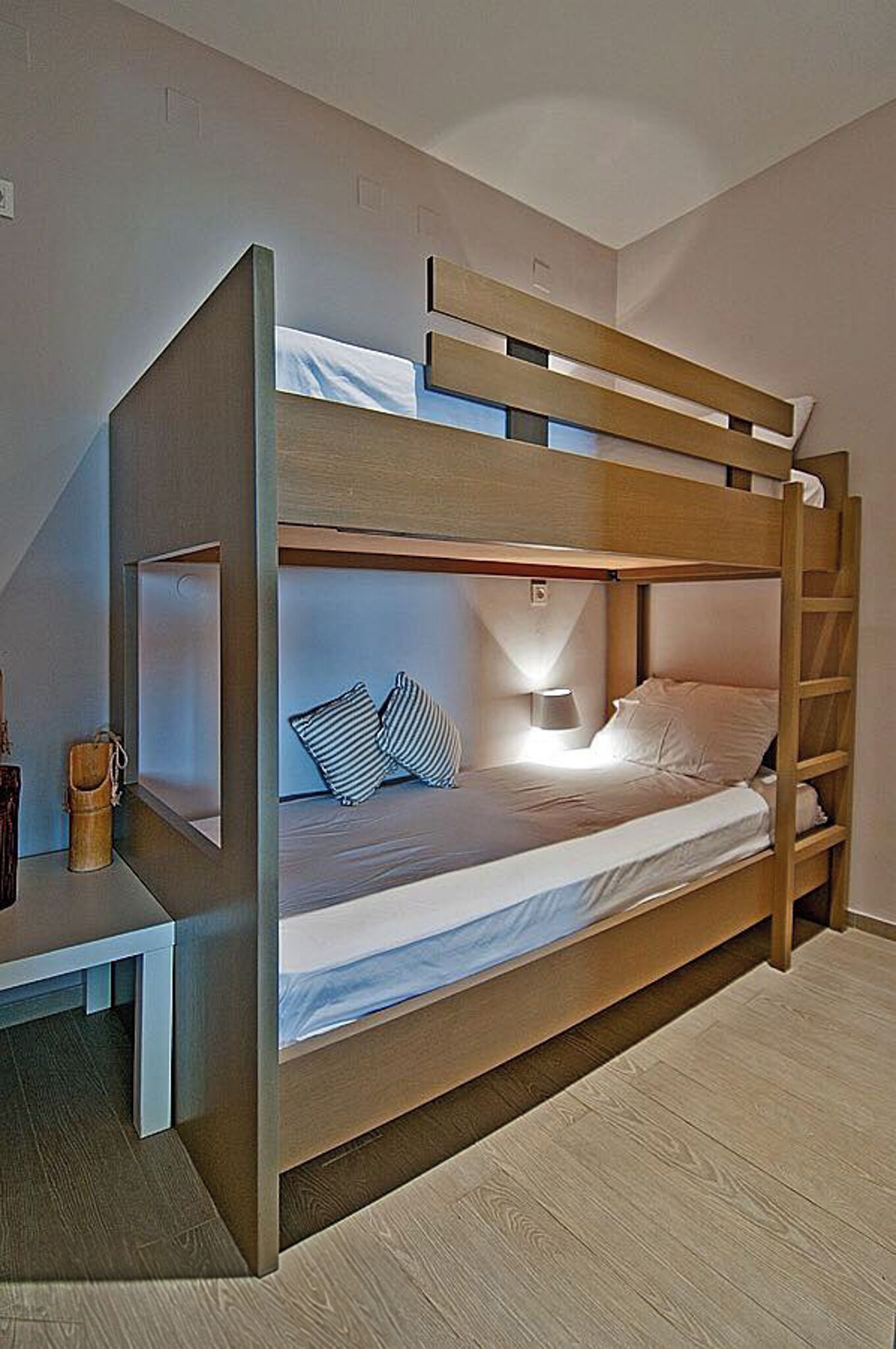 A bunk bed with a desk and lamp, wooden walls, and a window.