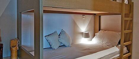 A bunk bed with a desk and lamp, wooden walls, and a window.