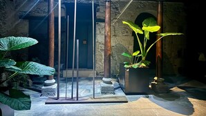 Interior de paredes de piedra con una estructura de columna de madera, una planta en maceta y un banco de piedra.