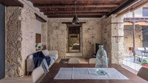 Una habitación rústica con paredes de piedra, techo de madera, un sofá, una mesa con una botella de vidrio y vistas a través de una ventana.