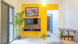 Una sala de estar con una pared de acento amarilla, televisor montado, sofá, mesa de centro y dos plantas en macetas.