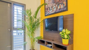 Una habitación con una televisión instalada en una pared de madera, una planta en maceta y una puerta con ventanal.