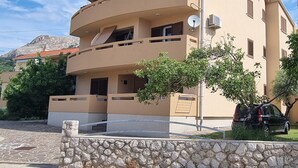 A multi-story building with balconies, a stone wall in front, and a car parked nearby.