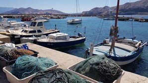 A marina with boats docked, fishing nets, and mountains in the background.