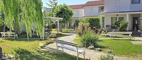 Een binnentuin met een bankje, een pergola en een pad dat naar een gebouw met een rode dakbedekking leidt.