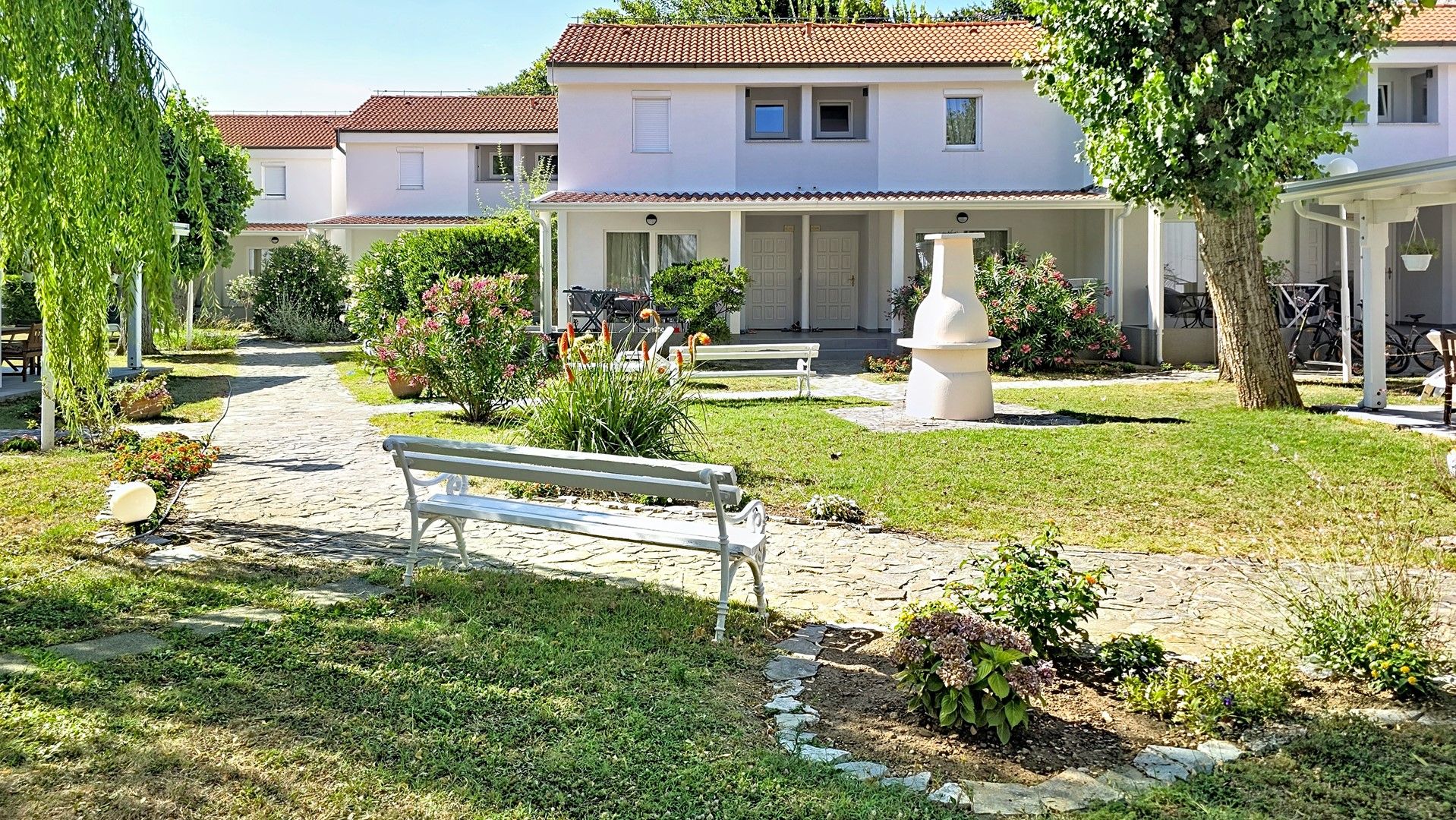 Un patio con un sendero adoquinado, bancos y un edificio blanco con techo de tejas.