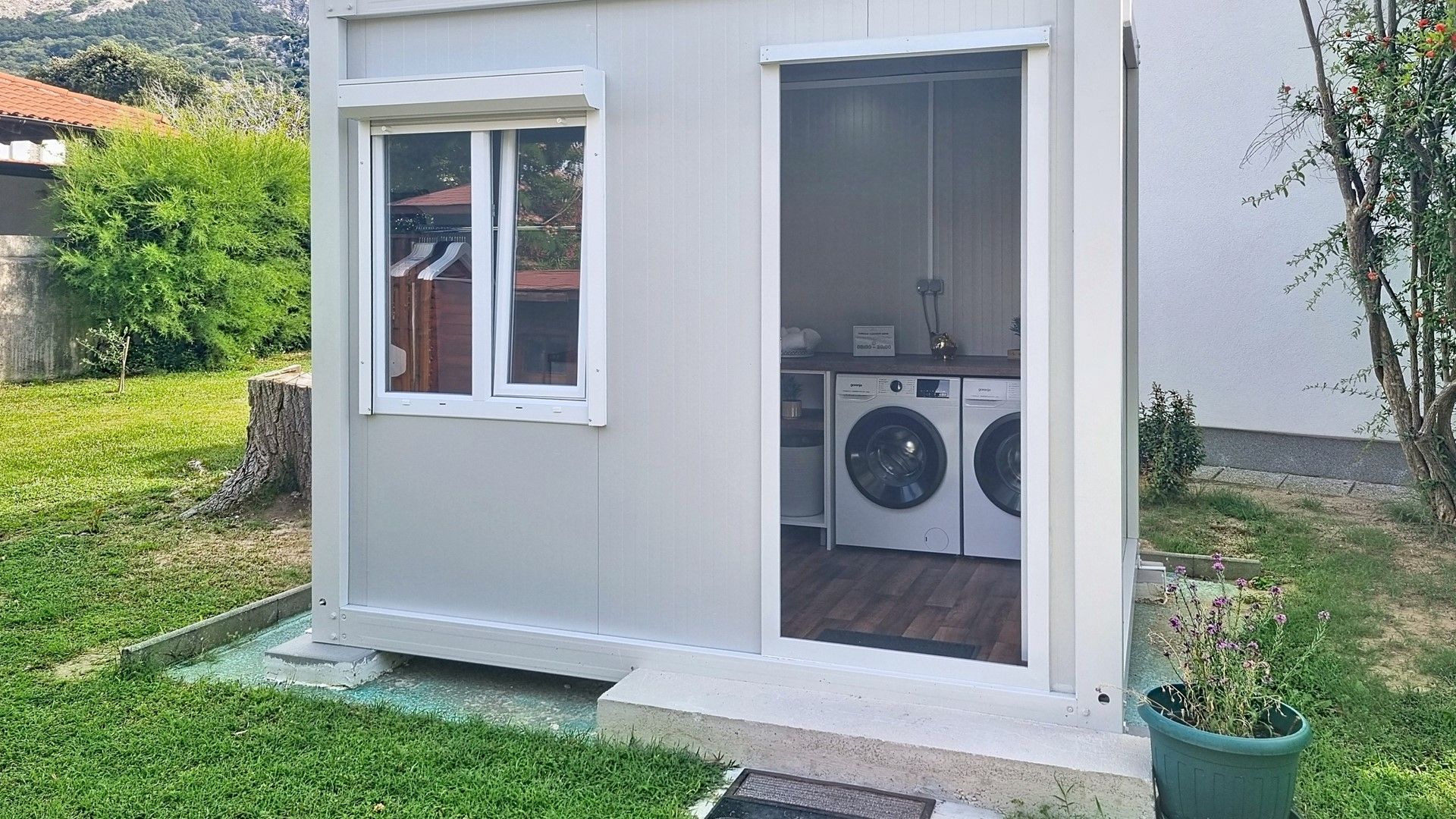 Un lavadero pequeño con lavadora y secadora, una ventana y una puerta que da a un área exterior cubierta.