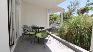 A balcony with a table and chairs, a glass door, and a view of greenery.