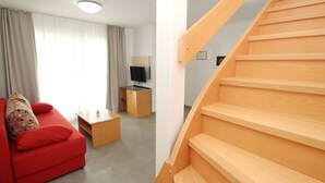 A modern living room with a red sofa, a wooden coffee table, a TV on a stand, and a staircase.