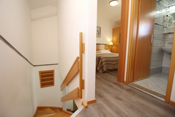 Una escalera conduce a un dormitorio con cama, un baño con ducha y una puerta de madera.