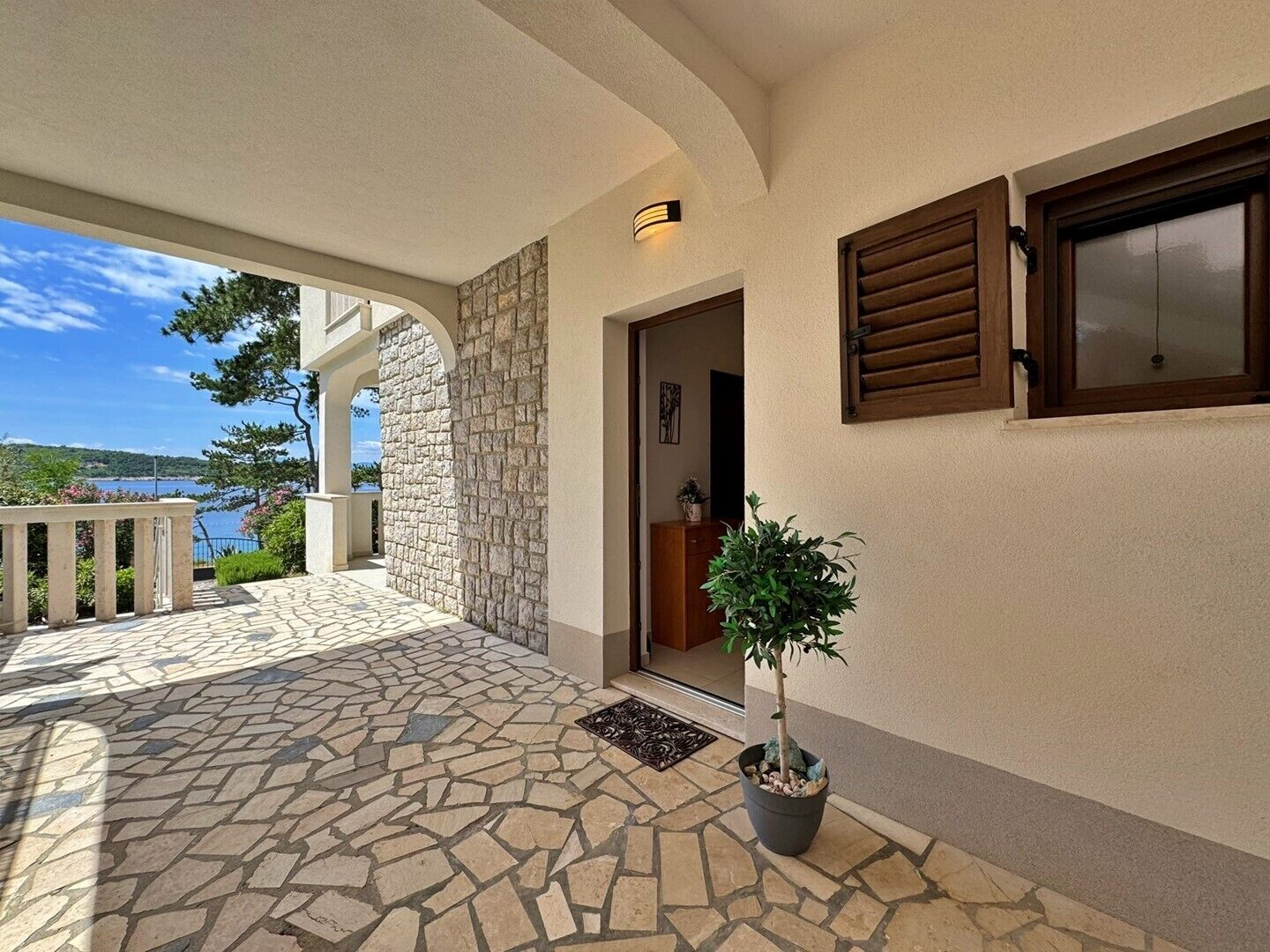 A stone-tiled patio with a potted plant, a wooden door, and a view of a lake.