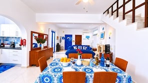 Une cuisine moderne avec des meubles blancs, un coin repas avec une nappe bleue à motifs, et un salon avec des canapés bleus.