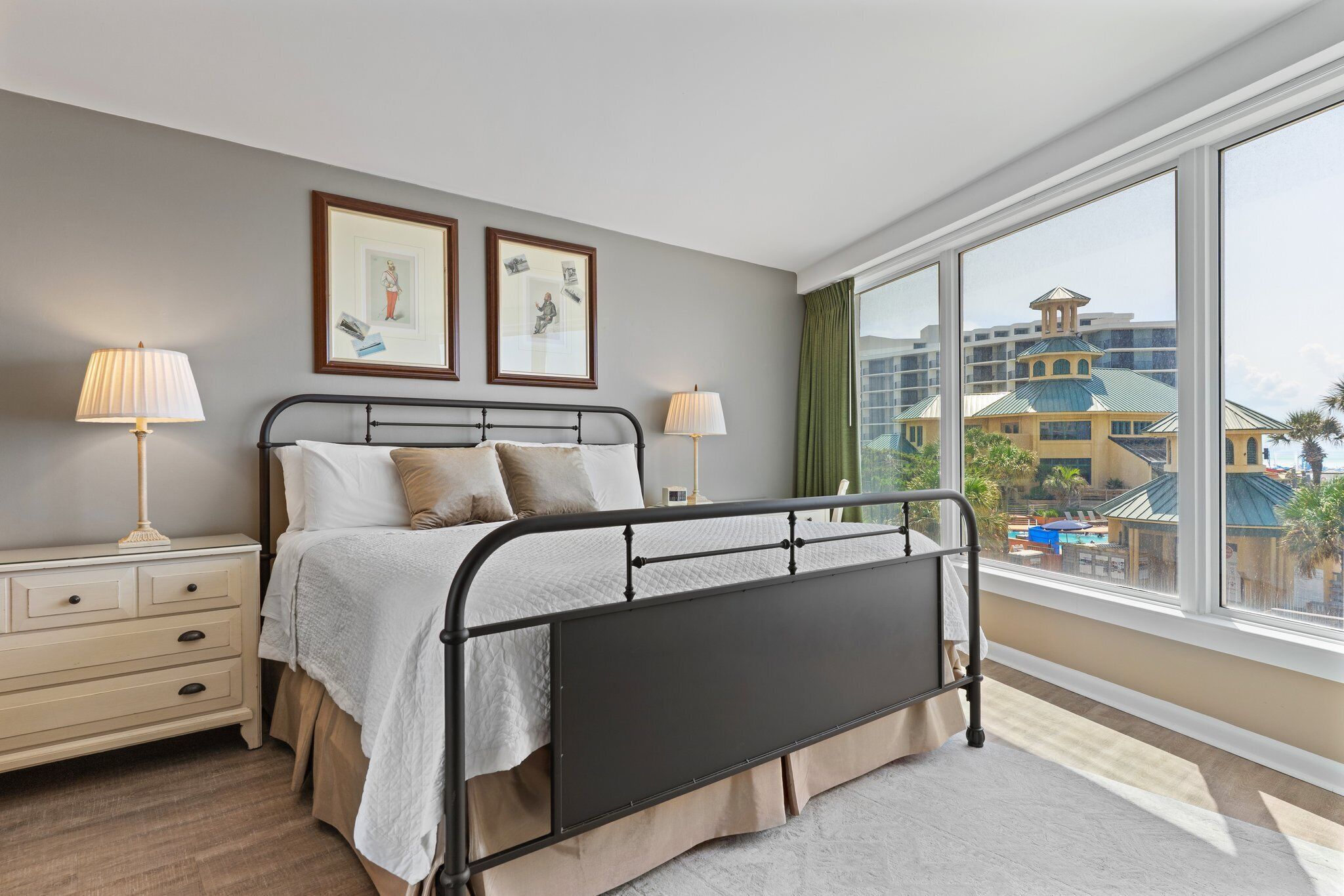 A hotel room with a bed, bedside tables, and a large window offering a view of a building with a green roof.