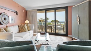 Ein Zimmer mit einem weißen Sofa, einem Glastisch und Blick auf einen Balkon mit Gartenmöbeln.