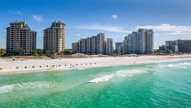 Ein Strandhotel mit mehreren Hochhäusern, einem Sandstrand und klarem, türkisblauem Wasser.