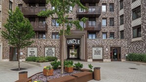 A multi-story building with a prominent "UNCLE" sign at the entrance, surrounded by landscaped areas and wooden planters.