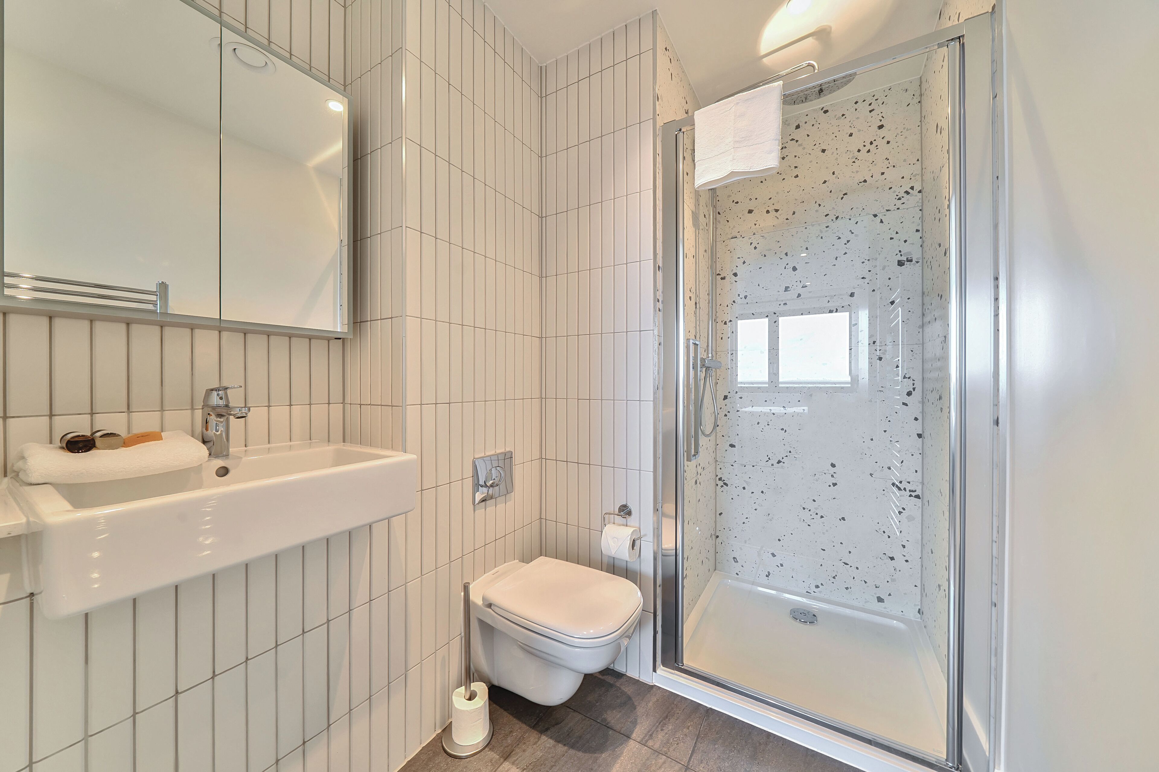 A modern bathroom with a white sink, toilet, and glass shower enclosure.
