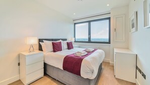 A modern bedroom with a bed, bedside tables, a window with a view, and a small cabinet.