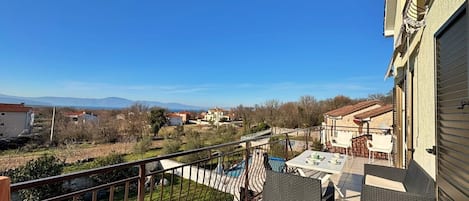 A balcony with a view of a swimming pool and distant houses.