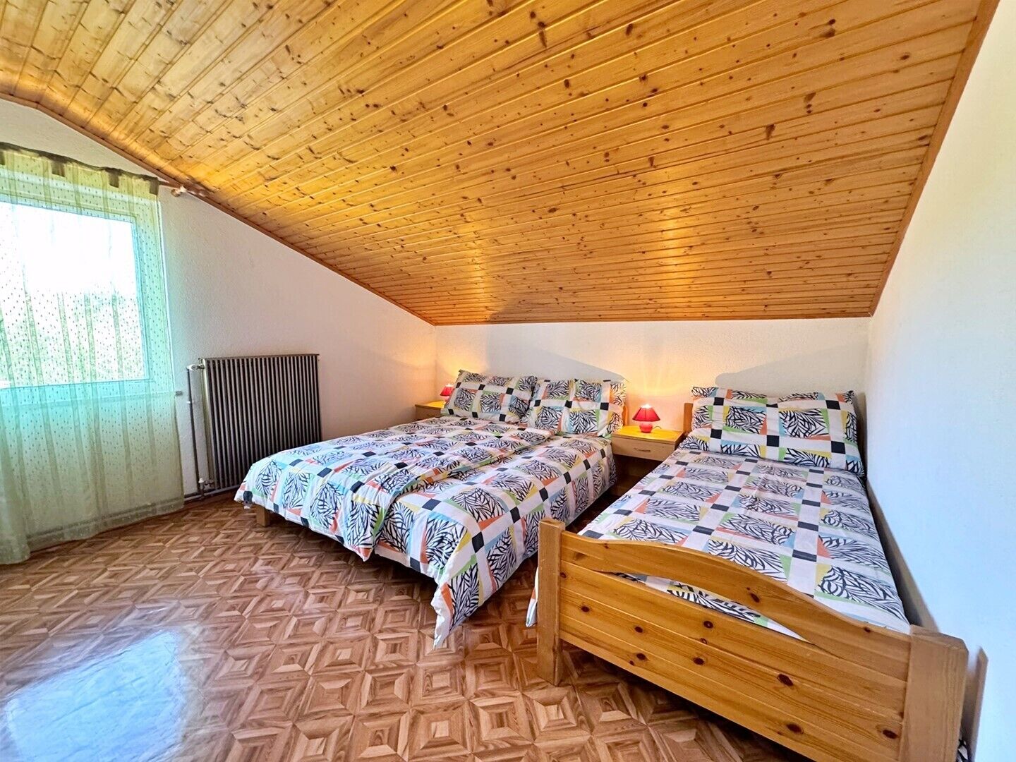 Ein Schlafzimmer mit zwei Holzbett, einem Heizkörper und einem Fenster mit durchsichtigen Vorhängen.