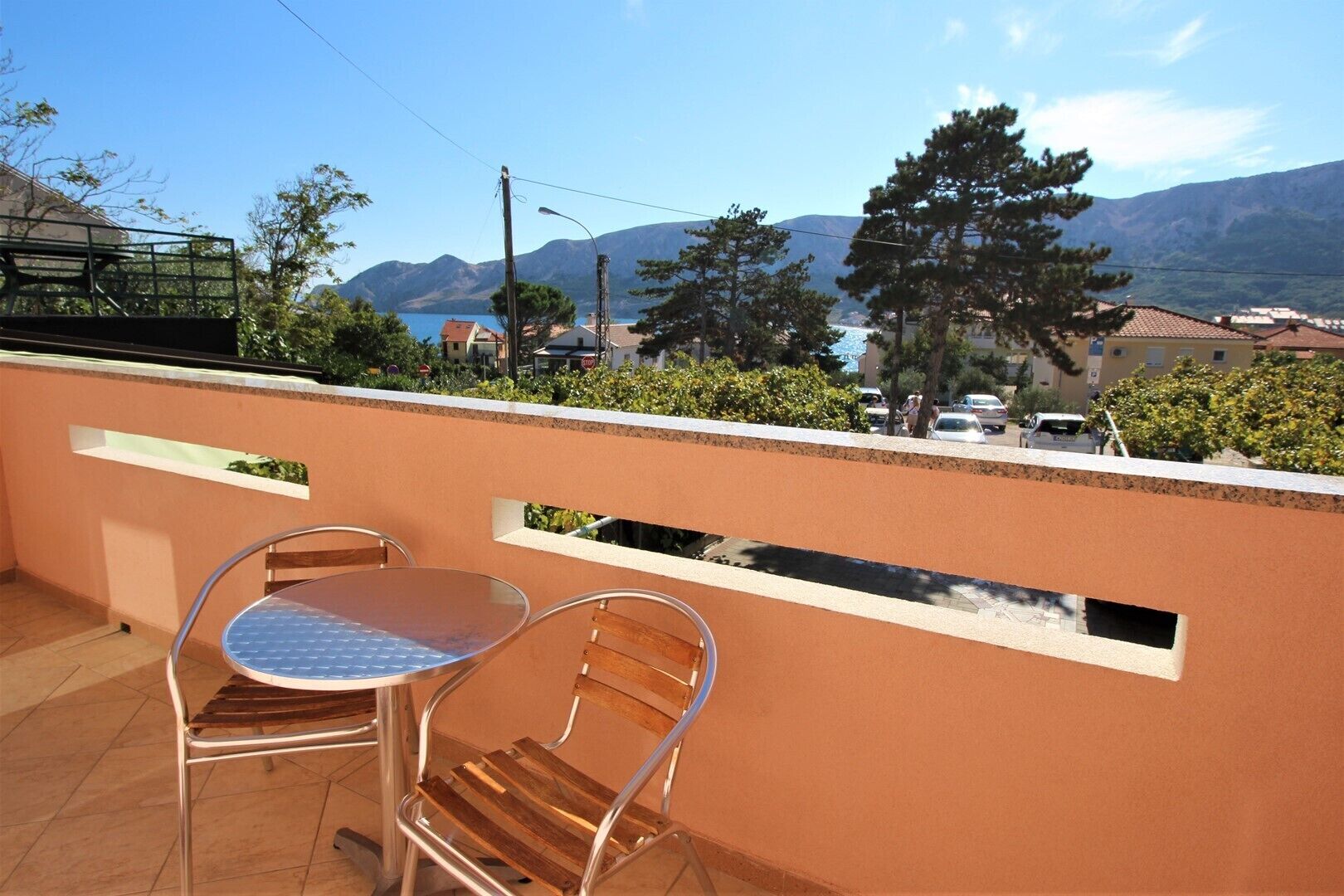 Un balcón con dos sillas y una mesa, con vistas a un paisaje montañoso bajo un cielo despejado.