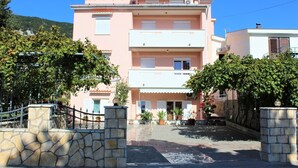A multi-story building with a stone entrance gate, potted plants, and a clear sky. - Apartment Lucijana No.2 - with Balcony, 150 m from the Beach (Baska)