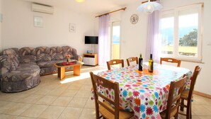A living room with a sofa, a TV, a dining table with chairs, and a view of the outdoors. - Apartment Lucijana No.4 - with Balcony, 150 m from the Beach (Baska)
