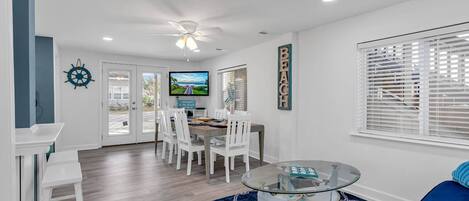 A modern dining area with a glass table, white chairs, and a blue patterned rug.