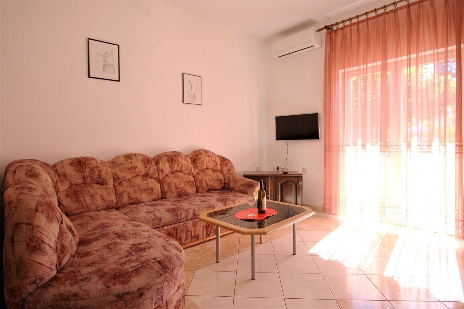 A living room with a sofa, a small table with a wine bottle, a TV, and a window with curtains.