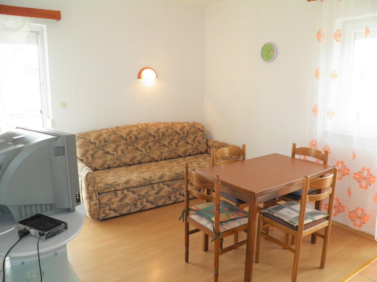Une pièce comprenant un canapé, une table à manger en bois avec des chaises, un téléviseur et une horloge au mur.