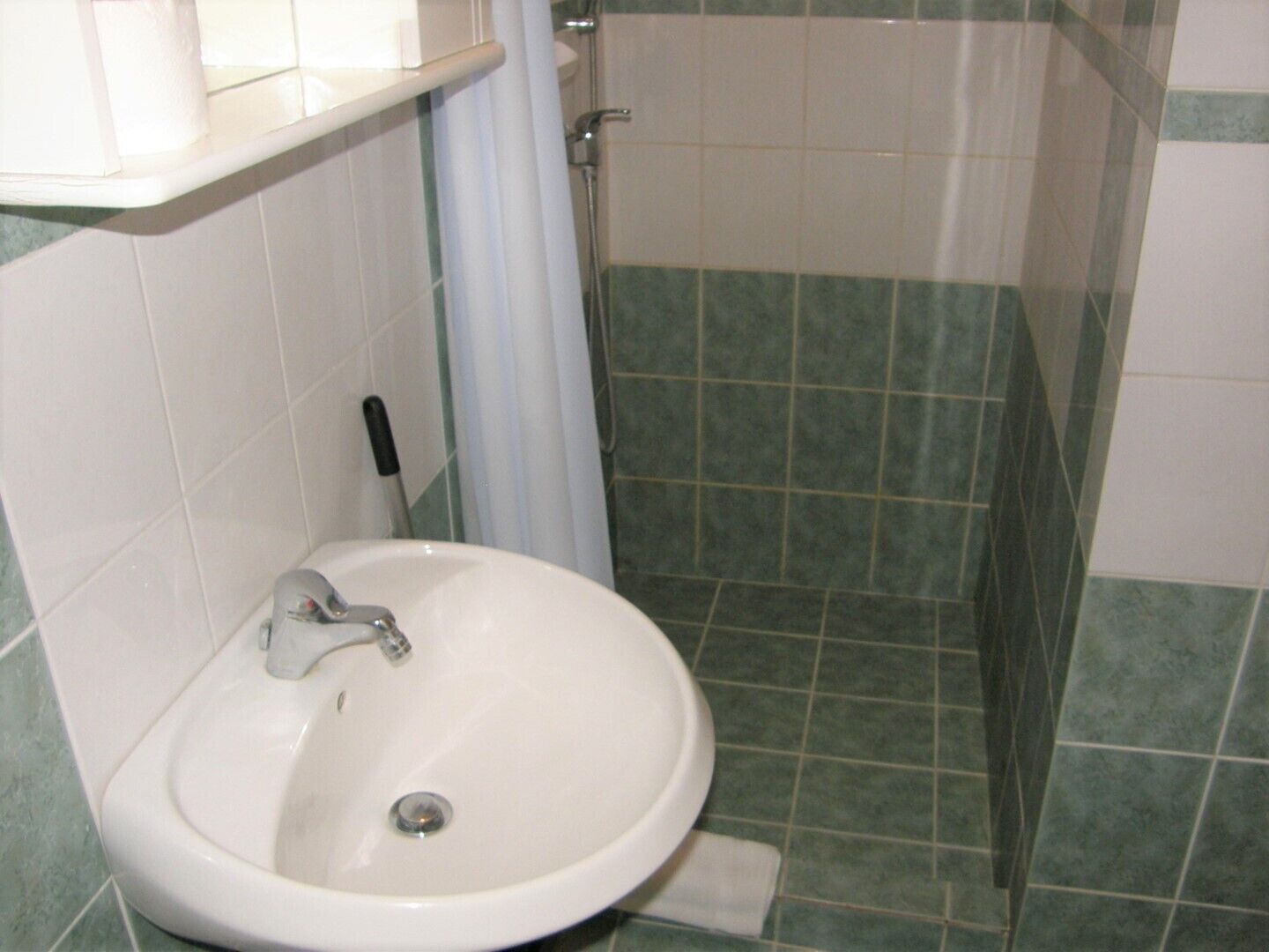 A bathroom with a white sink, a shower, and green-tiled walls.