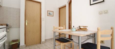 A small, clean room with a kitchenette, a wooden door, a framed picture on the wall, and a simple table with chairs.