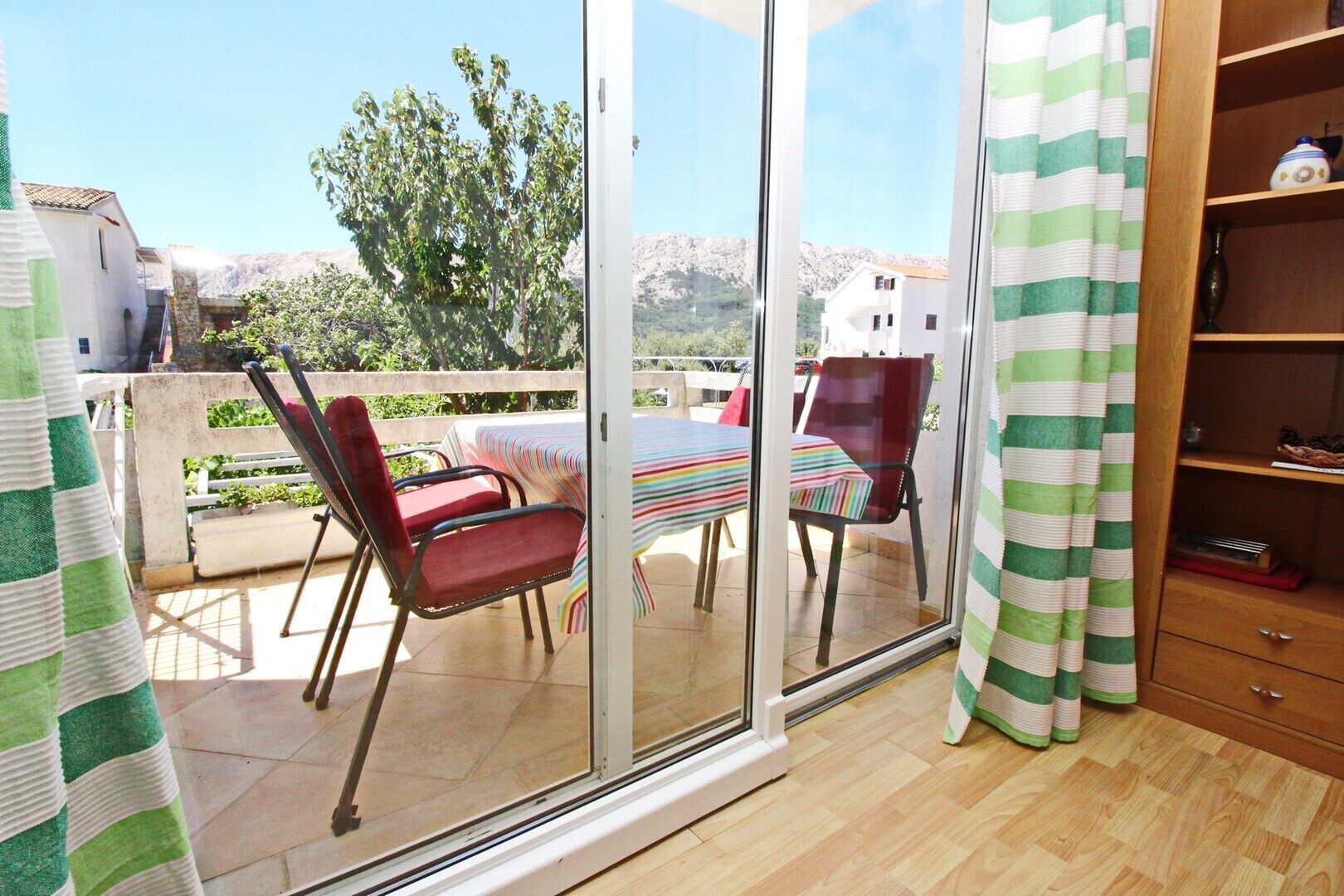 Ein Zimmer mit einer Glastür, die auf eine Außenpatio mit Tisch und Stühlen, einen Holzschrank und einen Blick auf einen Berg führt.