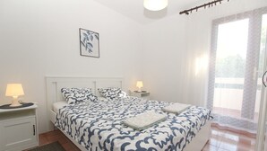 Ein Schlafzimmer mit einem großen Bett, zwei Nachttischen mit Lampen, einem gerahmten Kunstwerk an der Wand und Blick ins Freie durch ein Fenster.