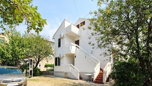 Un bâtiment à deux étages, à l’extérieur blanc, avec un escalier menant à l’étage supérieur et une voiture garée devant.