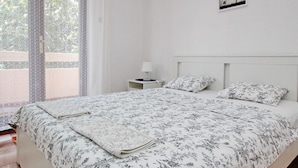 Un lit double avec une couvre-lit à motifs floraux, une table de chevet avec une lampe et une fenêtre agrémentée de rideaux à motifs.