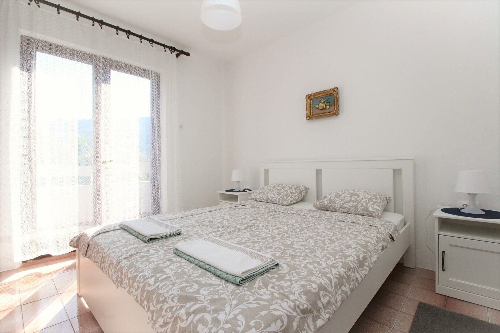 A bedroom with a bed, bedside tables, a nightstand, a lamp, and a picture frame on the wall.