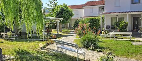 A courtyard with a bench, a pergola, and a pathway leading to a building with a red-tiled roof.