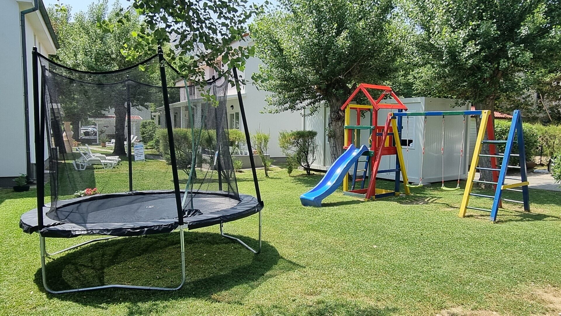 A trampoline, a slide, and a playhouse in a backyard.