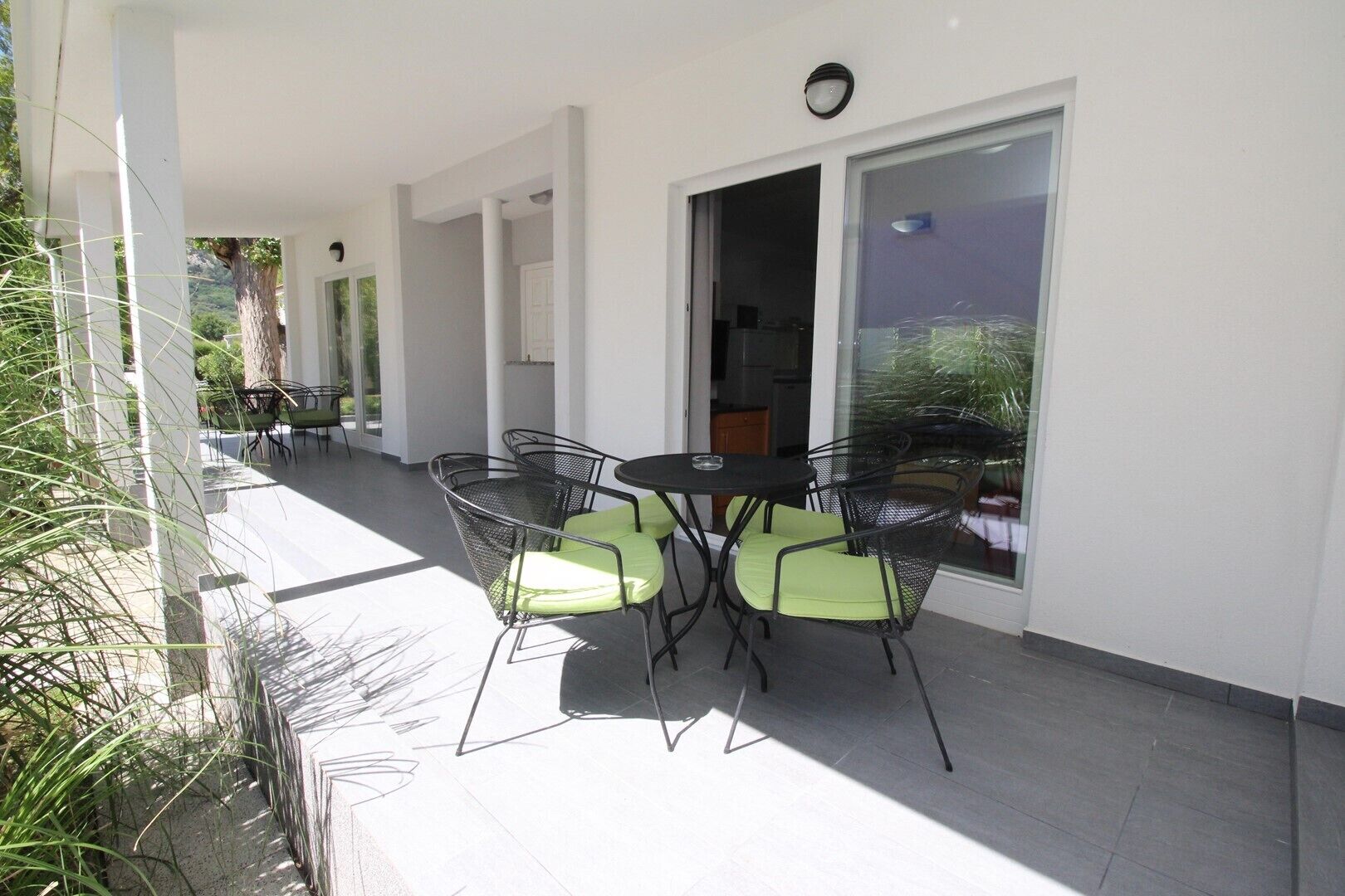 A covered patio with a table and chairs, large sliding glass doors, and a view of greenery.