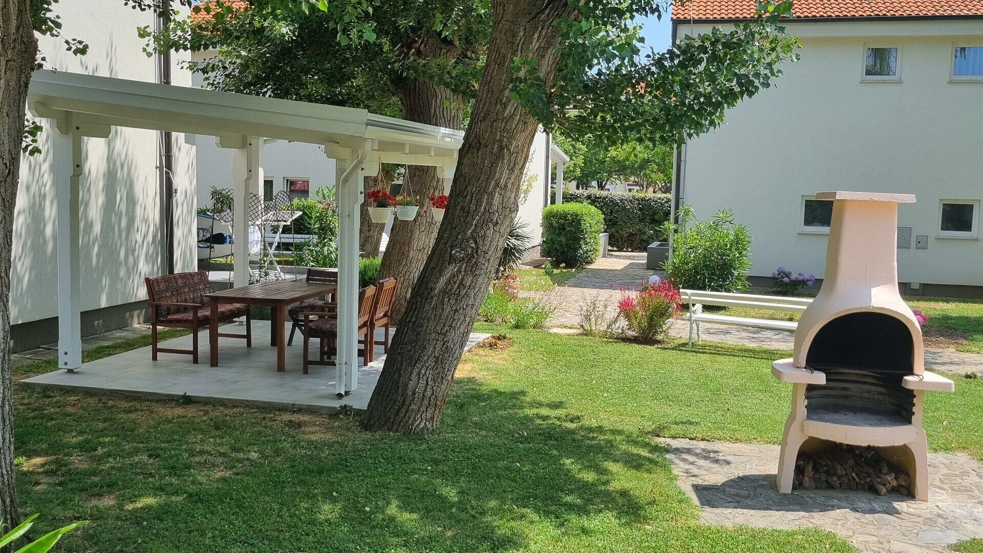 Un patio con tavolo e sedie, un pergolato, un albero e un forno a legna.